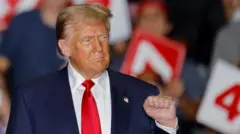 Trump ahagaze muri mitingi mu mujyi wa Greensboro, muri North Carolina, azamuye igipfunsi cye, ndetse abantu benshi bari inyuma mu buryo butagaragara neza bafite ibimenyetso bya ''47'' 