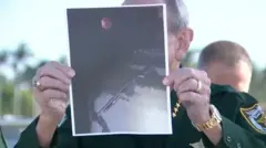 Шериф округа Палм-Бич Рик Брэдшоу показывает фотографию ружья подозреваемого, на которой на заднем плане видна красная канистра с бензином. 