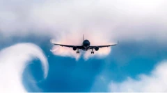 Bulutlar ve mavi gökyüzüyle çevrili havada inişe geçen bir uçak