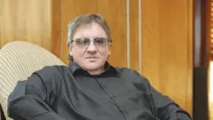 Well-known South African businessman Douw Steyn dey wear black shirt and glasses as e siddon for chair.