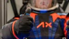 Homem em traje espacial faz joinha com a mão