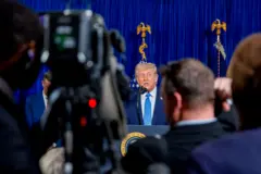 Trump de fondo. Delante, una cámara de televisión y varias personas.