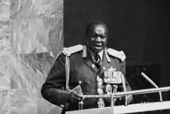 Imagen en blanco y negro del presidente de Uganda Idi Amin, quien viste un uniforme militar de mariscal de campo con muchas condecoraciones mientras habla desde el podio de la Asamblea General de la ONU.