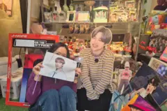 Yeon-su posa junto a productos de BTS en un café temático de BTS cerca de la sede de HYBE en Seúl.