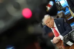 Trump compenetrado, sentado diante de sua mesa