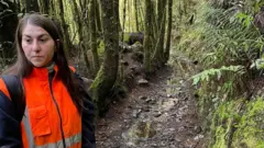 Justine, de cabelos longos castanho-escuros, veste uma jaqueta laranja de alta visibilidade em meio à floresta