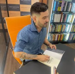 Brendo Silva firma un libro en un escritorio
