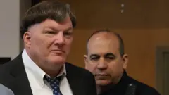 Фото чоловіка у костюмі, на задньому плані інший чоловік - поліцейський