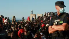 Migranți așteaptă la coadă pentru a primi alimente și băuturi oferite de Crucea Roșie, după traversările masive, pe uscat și pe mare, din Maroc către exclava spaniolă Ceuta, pe 3 august 2026.