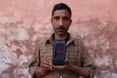 Govind Ram mostra uma foto, em seu telefone, de sua filha Surbhi Sharma, de 3 anos, que, junto com outras crianças, morreu devido a uma lesão renal após consumir um xarope para tosse contaminado em Jammu, entre dezembro de 2019 e janeiro de 2020, perto de um parque em Ramnagar, nos arredores de Jammu, Índia, em 28 de março de 2023.