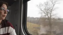 دختری که عینک به چشم دارد از کلکین قطار به بیرون نگاه می‌کند.