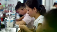 A woman sits at a sewing machine in a factory