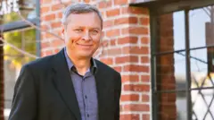 O corretor de imóveis Matthew Goulden tira fotos em frente a um prédio de tijolos vermelhos.