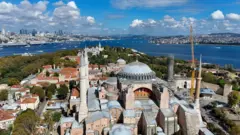 نمایی از مسجد ایا صوفیه استانبول در یک روز آفتابی با پس زمینه دریای آبی‌رنگ.