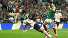 يظهر لاعب المنتخب الإنجليزي بلباس فريقه الأبيض والكحلي وهو يقفز باتجاه الكرة ليضربها برأسه وخلفه لاعبان من فريق المكسيك بلباس الفريق الأخضر والأبيض، يحاول أحدهما منعه من تسديد الكرة.