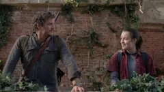 The Last of Us dizisinin başrollerindeki Pedro Pascal ve Bella Ramsey diziden bir sahnede, duvar önünde birbirlerine bakıyorlar.