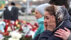 A woman clutches her hands to her face in shock in front of flowers to commemorate those killed in the Moscow concert hall attack