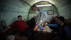 Macdan qode Eemin Xasan (dhexda) ku jira iyo saaxiibadiis oo afur ku wadaagaya aqal yar oo ay ku dhisteen godka dhexdiisa