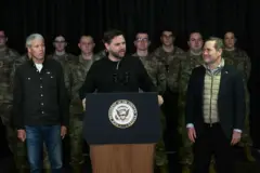 Vance discursando em palanque, rodeado por outros homens e militares