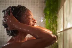 Jeune femme africaine prend une douche, se lavant les cheveux. 