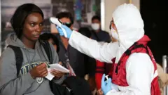 Personal de salud de Ecuador toma la temperatura de pasajeros en el aeropuerto.