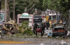 varios policías cargan un cuerpo en unas mantas. caminan entre escombros luego de la explosión en cali, colombia.