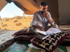رجل في منتصف العمر يجلس في خيمته يصحح أوراق الامتحانات.