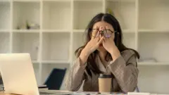Жінка сидить перед комп'ютером і втомлено тре очі