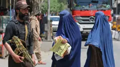 دو زن افغان برقع‌پوش از کنار یکی از نیروهای امنیتی طالبان در خیابانی در شهر جلال‌آبادعبور می‌کنند