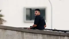 कालो टीशर्ट लगाएका र हातमा बन्दुक बोकेका एक युवक।