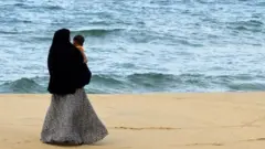 In this picture taken on April 25, 2019, a Sri Lankan Muslim woman walks along a beach with her child in Kattankudy. - Zahran Hashim's sword-wielding zealotry fuelled fears in the sleepy east coast town of Kattankudy long before the cleric became Sri Lanka's most wanted man over the horrific Easter Sunday suicide attacks. The country's president announced on April 26 that Hashim led and died in the attack on the Shangri-La hotel in Colombo -- one of three hotels and three churches hit by bombers wearing explosive backpacks.