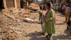 Mulheres caminham em direção à sua casa destruída, após a operação militar do Paquistão contra a Índia, em Rehari, Jammu.