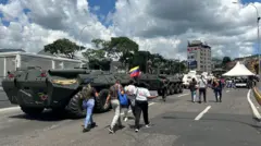 Em uma rua de Caracas, tanques militares se deslocam ao lado de pessoas vestidas à civil.