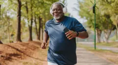 An elderly Black man dey run wit headphones and  mobile phone for im hand
