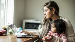 Mulher está usando o computador com uma mão, enquanto na outra ela segura uma criança que está no colo