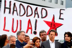 Fotografia colorida mostra uma faixa com a frase "Haddad e Lula! 13" ao fundo e diferentes pessoas da política brasileira no plano à frente, como Fernando Haddad, Manuela d'Ávila, Lindbergh Farias e Ana Estela Haddad