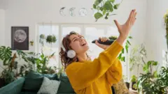 Joven cantando con un control remoto como micrófono