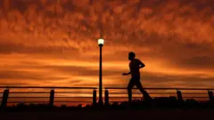 Pessoa correndo com céu laranja, de por do sol, ao fundo