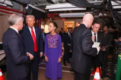 Carney, Trump y Sheinbaum están detrás del escenario durante el evento de la FIFA que se ofició en diciembre. Carney está hablando mientras Trump y Sheinbaum lo miran con atención.