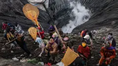 A group of people stand on the edge of a volcano with long nets
