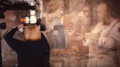 A restauradora com um equipamento nas mãos, trabalhando na restauração do mural