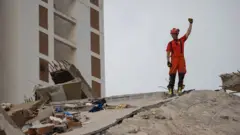 Spasilac maše rukom na srušenim zidovima bivše zgrade
