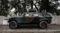 Un véhicule blindé est positionné à l'entrée d'une route bloquée à côté de la télévision nationale, Bénin TV, à Cotonou, le 8 décembre 2025.