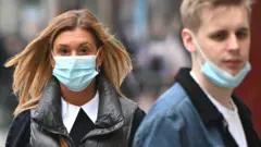 ጭምብል አድርገው በመንገድ ላይ የሚታዩ ሰዎች