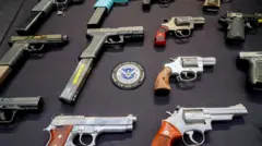 Unas doce armas cortas sobre una mesa negra y en el centro está el escudo de U.S. Department of Homeland Secutiry. New York City