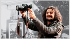 Fotoğrafta Hakan Tosun elinde bir fotoğraf makinesi tutuyor. 