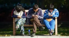 Мобил телефонига қараб ўтирган ёш хитойликлар