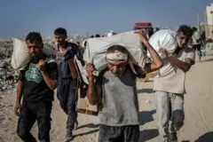 Hombres palestinos cubiertos de polvo cargan sacos en el paso de Zikim.