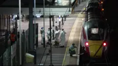 Trem na estação com pessoas vestindo macacões brancos forenses.