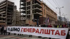 Протестующие с большим плакатом «Не дамо генералштаб» на фоне разрушенных зданий.